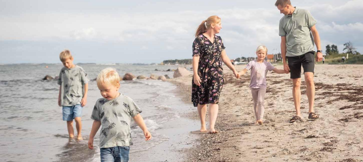 Familie med tre børn går tur på stranden