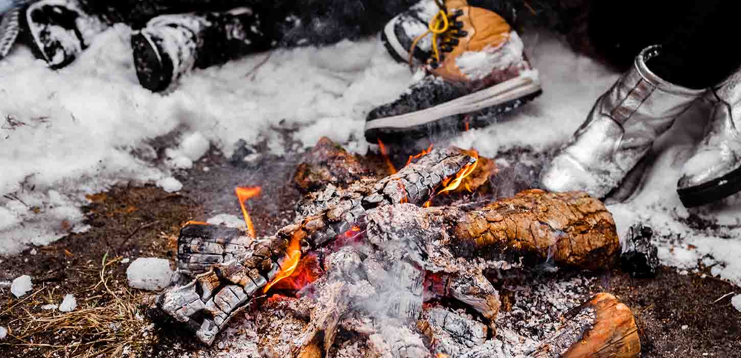 People sit with big boots by the lit fire in a snowy winter