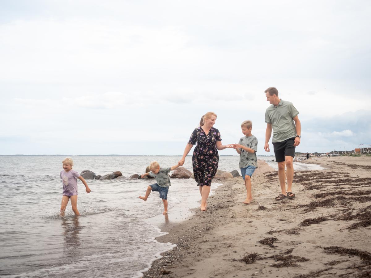 Familie går tur på stranden i sommertid ved Hasmark - tre børn