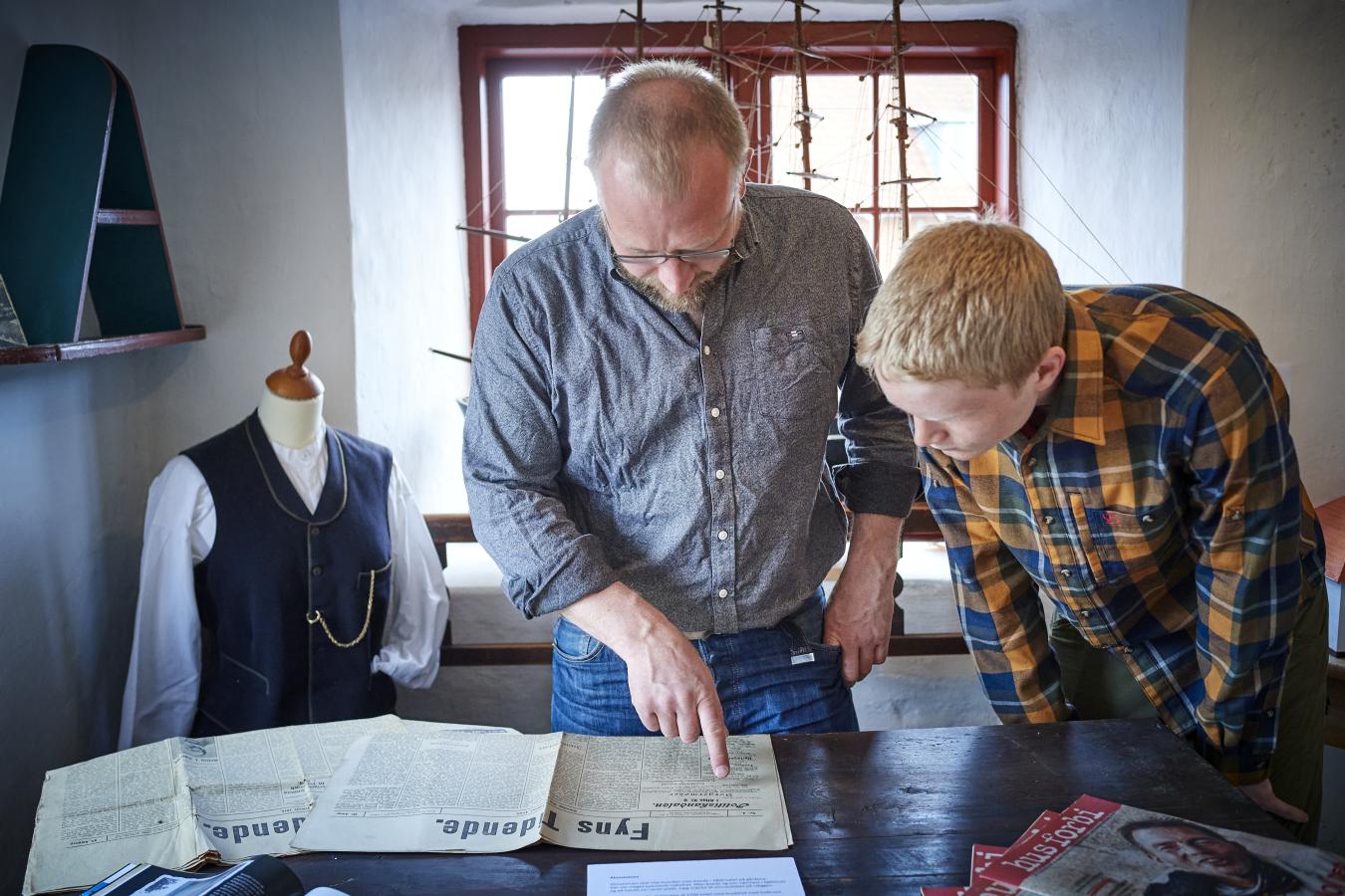 To museumsgæster - far og søn - på Otterup Museum kigger i gamle aviser