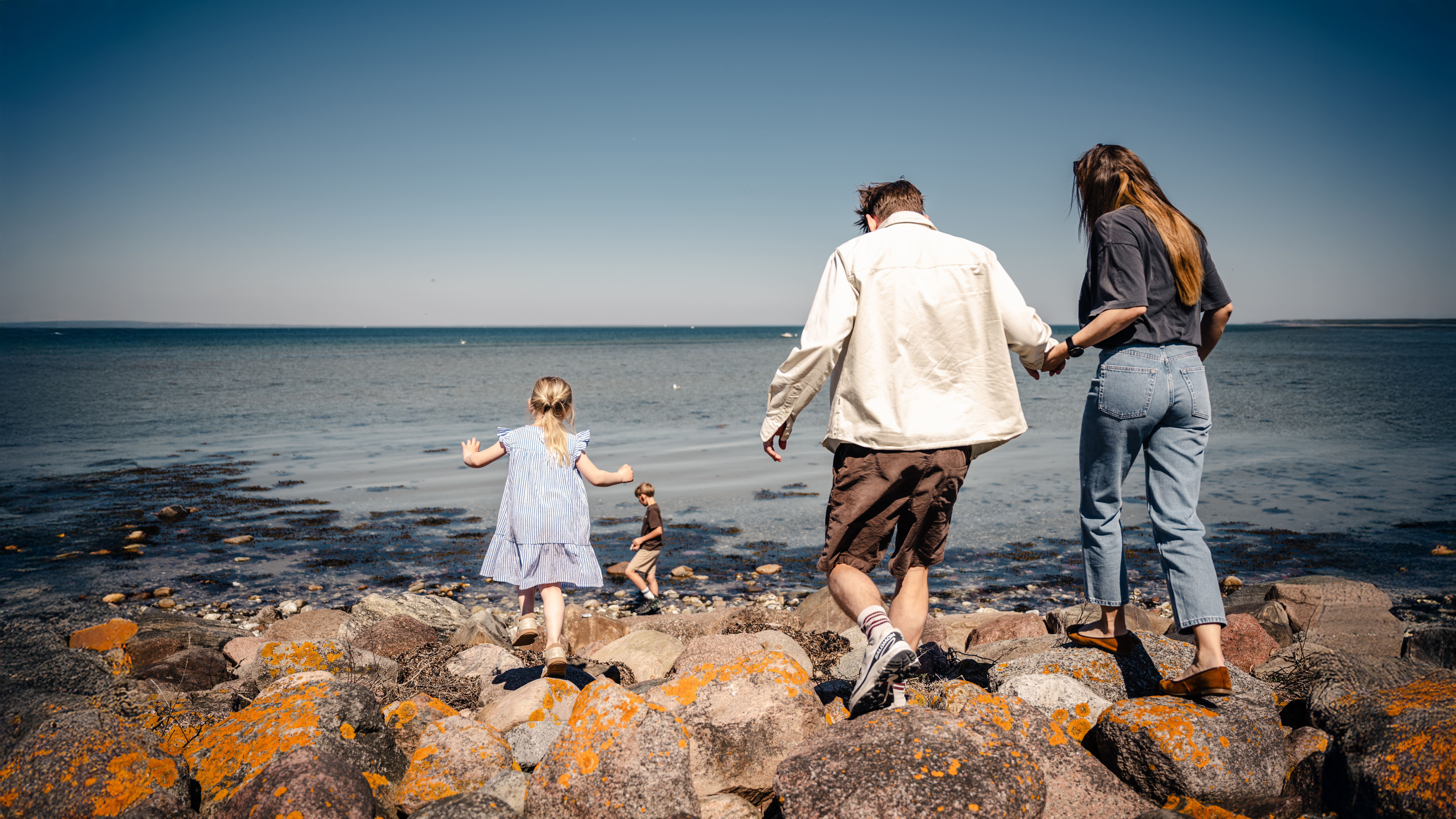 Familie går tur på stenene langs stranden ved Bogense kyst