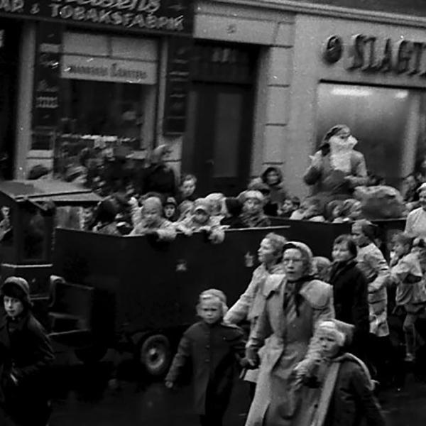 A large car with goblins drives past the shops in the main street - in 1955