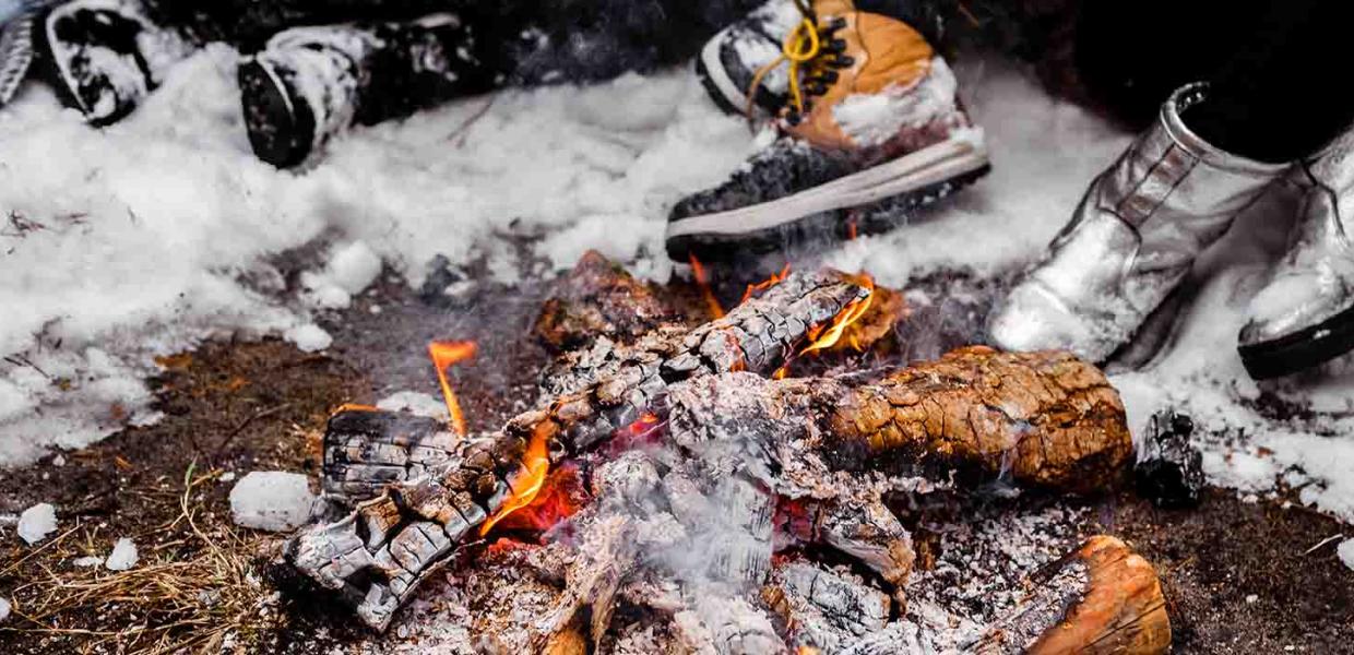 People sit with big boots by the lit fire in a snowy winter