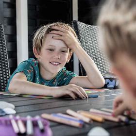 Dreng smiler til sin søster ved bordet i sommerhuset